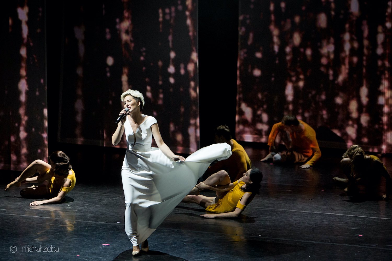 Widowisko Święty z Wadowic - Jan Paweł drugi. 
Scena Opery Krakowskiej. Wokalistka Magda Steczkowska oraz piątka tancerzy. Magda idzie przez scenę. Ma krótkie blond włosy. Ubrana jest w białą, długą do kostek suknię. Lewą ręką trzyma rozwianą suknię. Cztery tancerki i tancerz leżą na scenie. Opierają się o ziemię lewymi łokciami. Prawą ręką trzymają prawą nogę zgiętą w kolanie. Tancerki mają żółte, krótkie sukienki. Tancerz - żółtą bluzę i szary dres. W głębi sceny wiszą pasy tkanin wysokie na kilka metrów. Na nich wyświetlają się jasne nieregularne plamy.